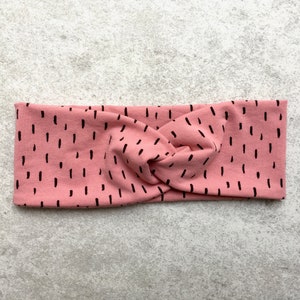 Könnte beinhalten: Ein rosa geknüpftes Stirnband mit einem schwarzen abstrakten Muster.
