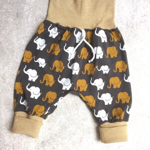 K&ouml;nnte beinhalten: Graue Babyhose mit einem gelben und wei&szlig;en Elefantenmuster. Die Hose hat einen breiten elastischen Bund mit gelben Streifen und einen Kordelzug.