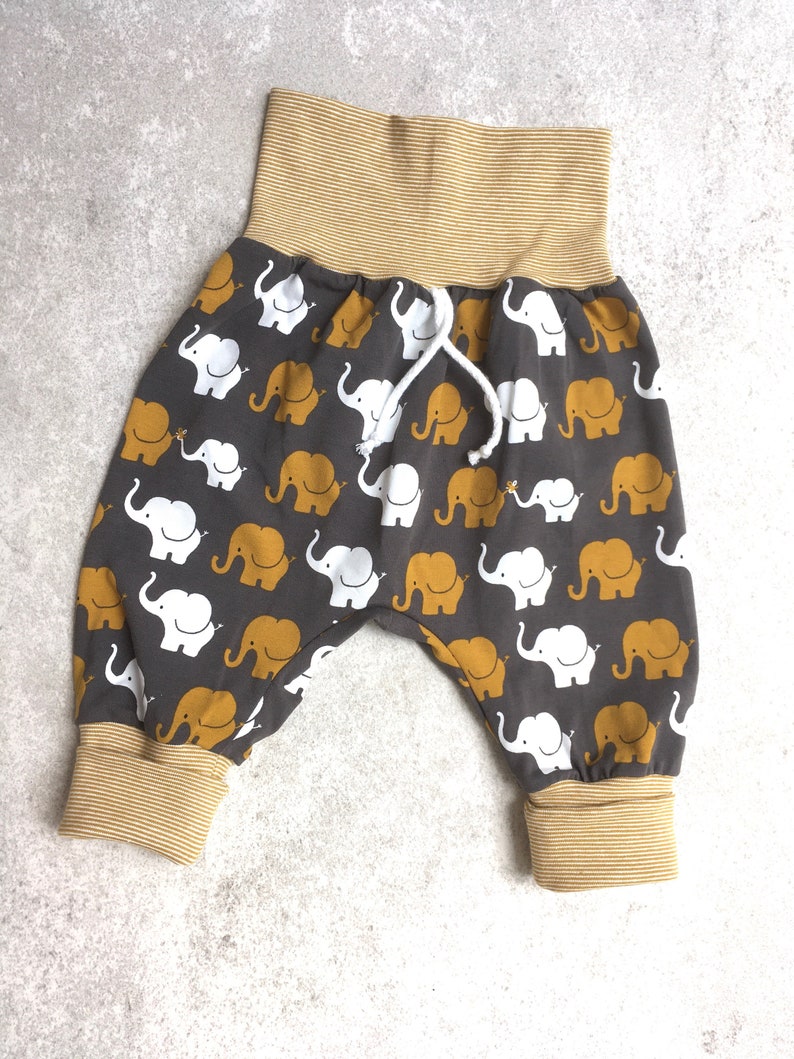 K&ouml;nnte beinhalten: Graue Babyhose mit einem gelben und wei&szlig;en Elefantenmuster. Die Hose hat einen breiten elastischen Bund mit gelben Streifen und einen Kordelzug.
