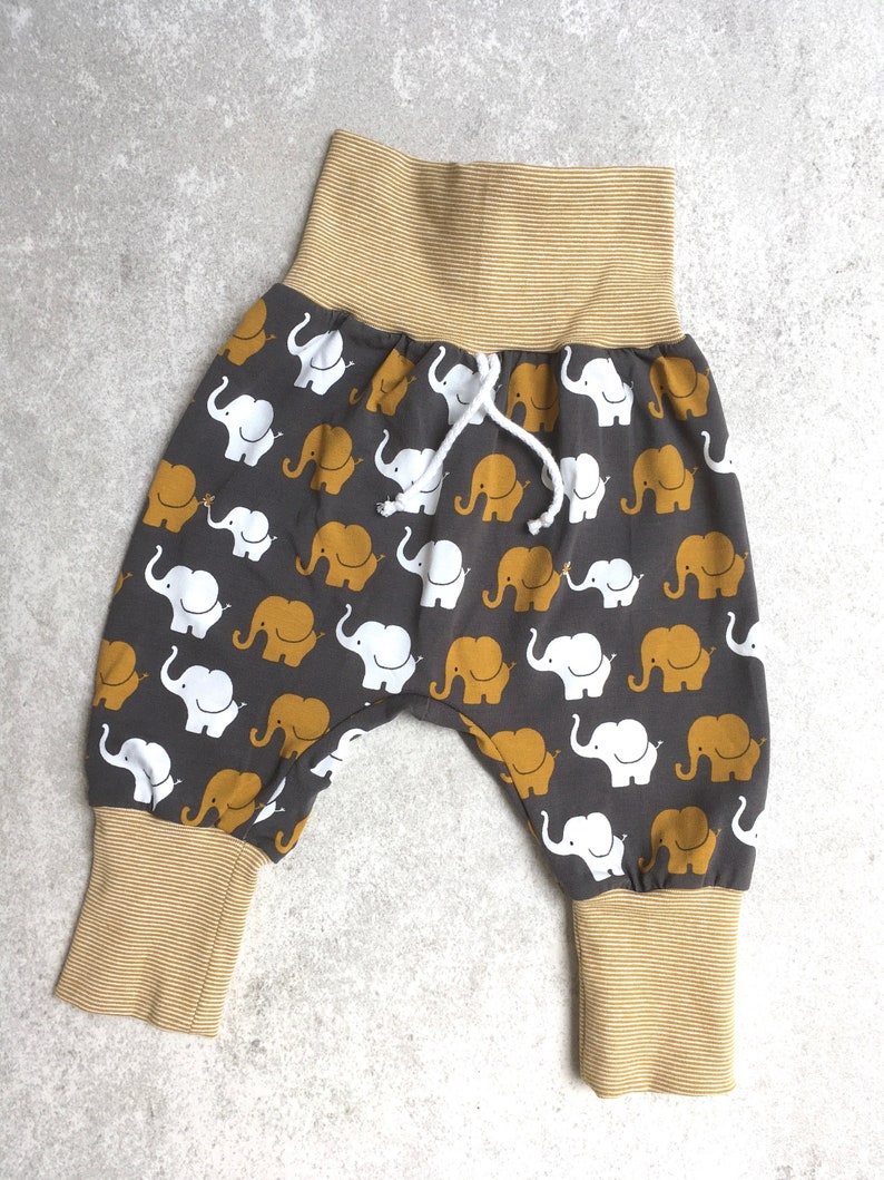 K&ouml;nnte beinhalten: Graue Babyhose mit einem wei&szlig;en und gelben Elefantenmuster. Die Hose hat einen gelben elastischen Bund und B&uuml;ndchen.
