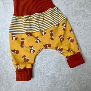 May include: A pair of yellow and brown baby pants with a fox print. The pants have a wide elastic waistband and cuffed legs.