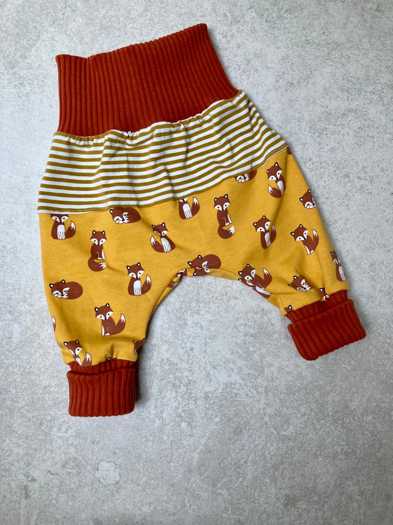 May include: A pair of yellow and brown baby pants with a fox print. The pants have a wide elastic waistband and cuffed legs.