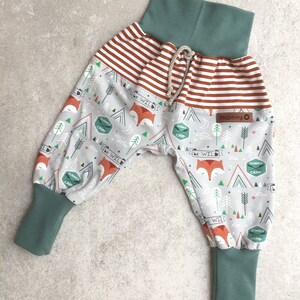 May include: Gray and white patterned pants with a fox print and the text "be wild". The pants have a brown and white striped waistband and teal blue cuffs.