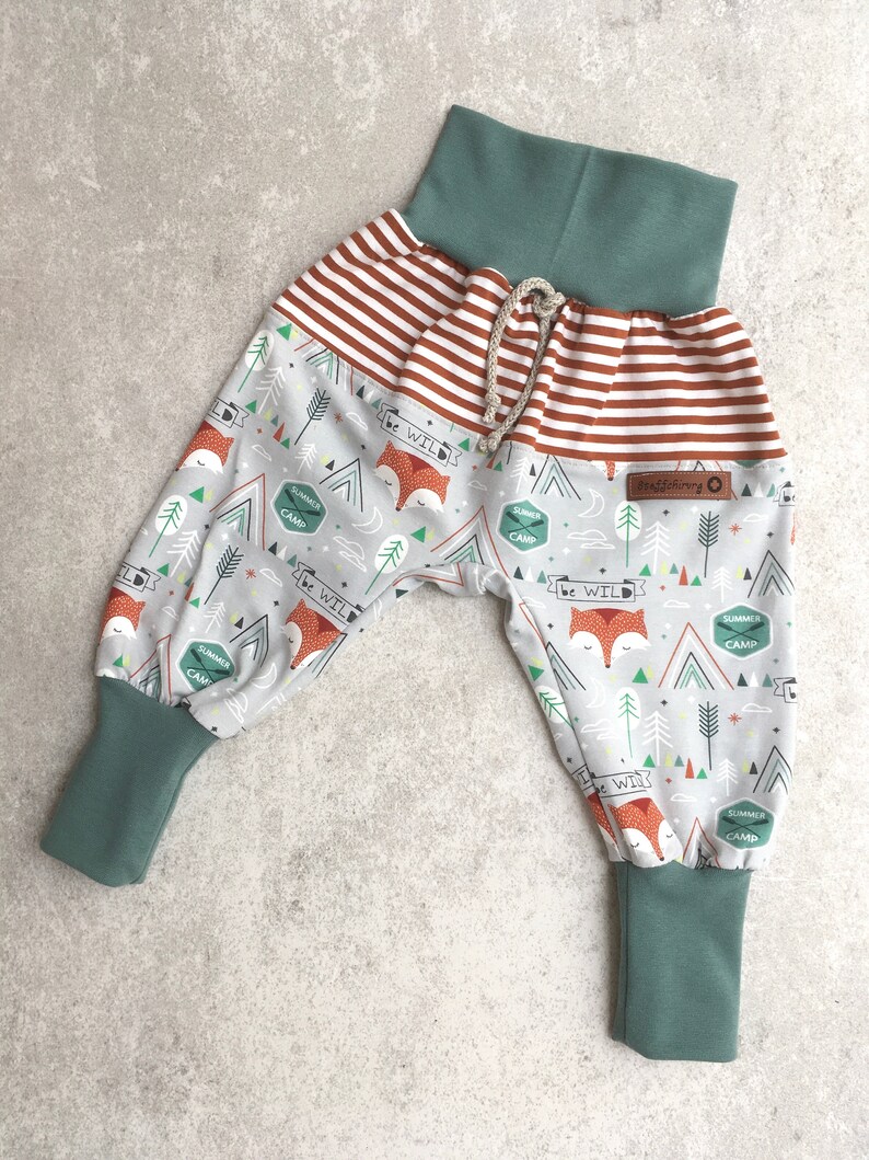 May include: Gray and white patterned pants with a fox print and the text "be wild". The pants have a brown and white striped waistband and teal blue cuffs.