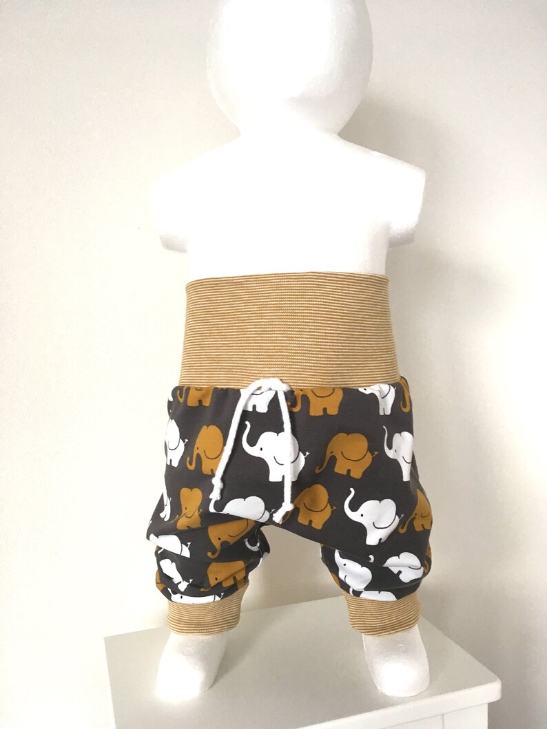 K&ouml;nnte beinhalten: Graue Babyhose mit einem wei&szlig;en und senfgelben Elefantenmuster. Die Hose hat einen senfgelben elastischen Bund und B&uuml;ndchen.