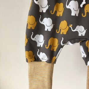 K&ouml;nnte beinhalten: Graue Babyhose mit einem Muster aus wei&szlig;en und gelben Elefanten. Die Hose hat einen braunen, gestreiften Bund.