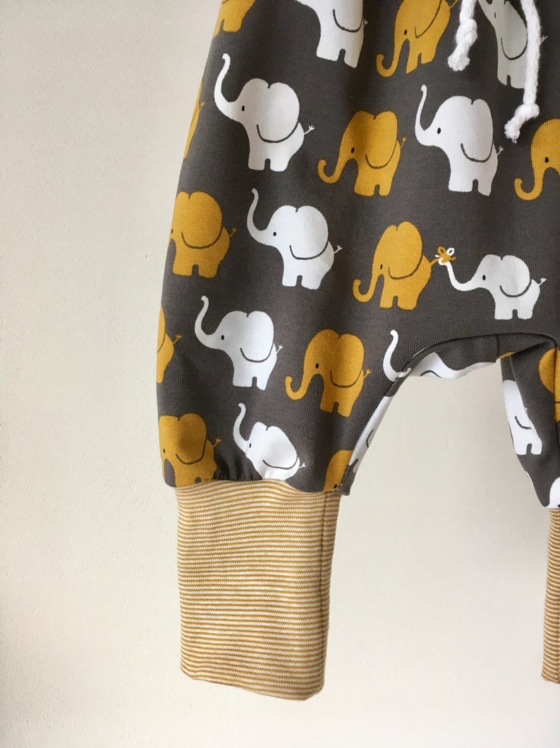 K&ouml;nnte beinhalten: Graue Babyhose mit einem Muster aus wei&szlig;en und gelben Elefanten. Die Hose hat einen braunen, gestreiften Bund.