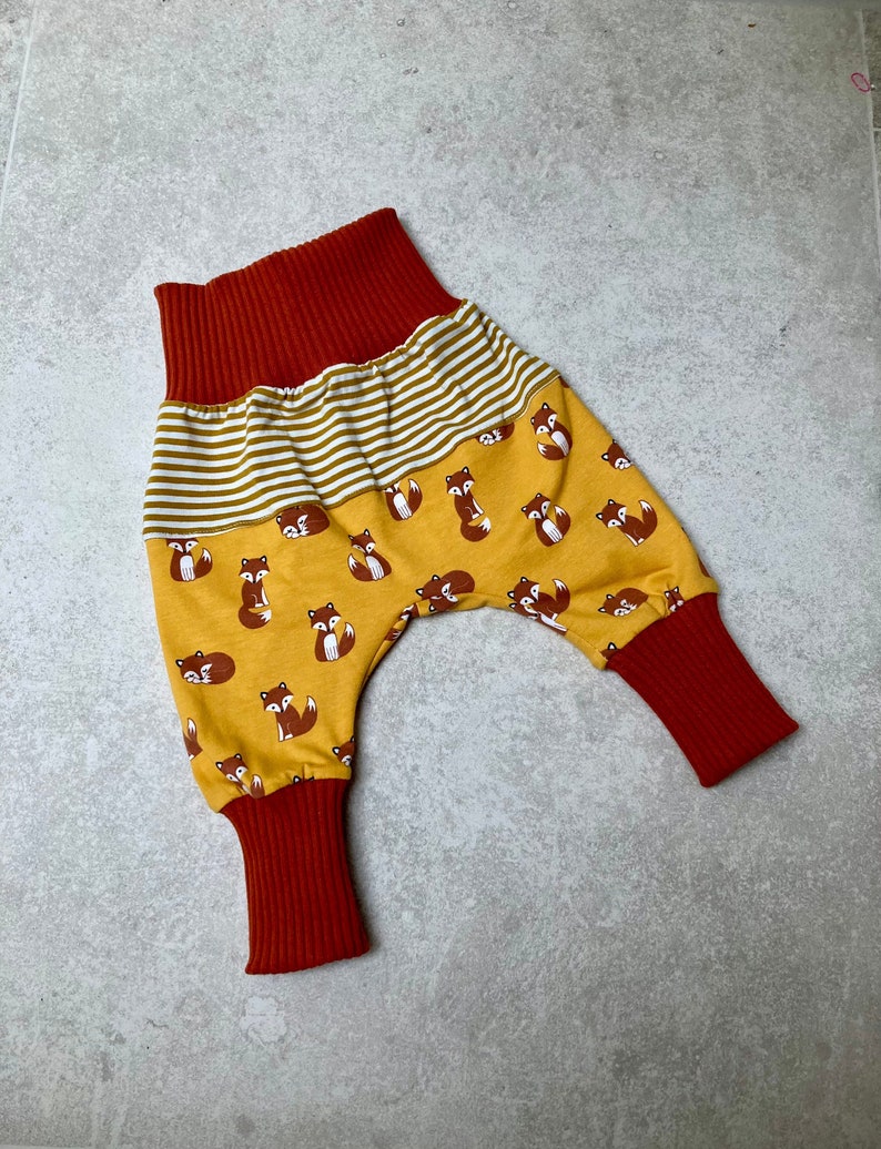 May include: Red and yellow baby pants with a fox print. The pants have a wide elastic waistband and cuffed legs.
