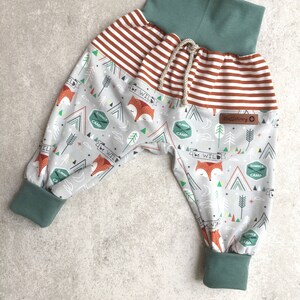 May include: Gray and white patterned pants with a red and white striped waistband and green cuffs. The pants have a fox and camping themed print with the text "be wild" and "summer camp".