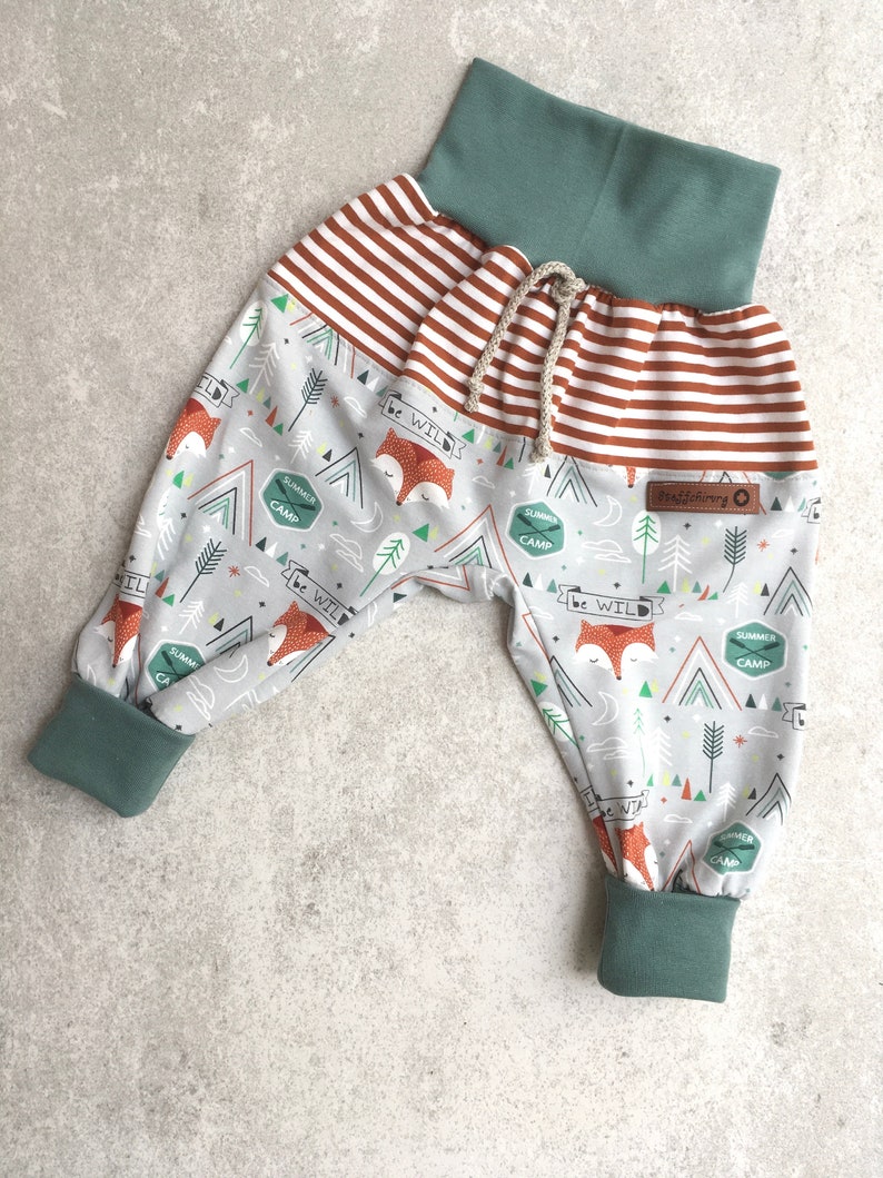 May include: Gray and white patterned pants with a red and white striped waistband and green cuffs. The pants have a fox and camping themed print with the text "be wild" and "summer camp".
