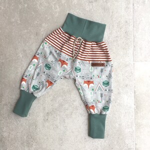 May include: Gray and white patterned pants with a red and white striped waistband. The pants have a drawstring and green cuffs. The pattern features foxes, trees, and the words "Be Wild" and "Summer Camp".