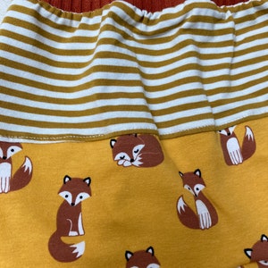 May include: Mustard yellow fabric with a repeating pattern of brown foxes. The fabric has a white and mustard yellow striped band at the top.