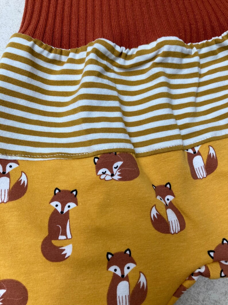 May include: Mustard yellow fabric with a repeating pattern of brown foxes. The fabric has a white and mustard yellow striped band at the top.