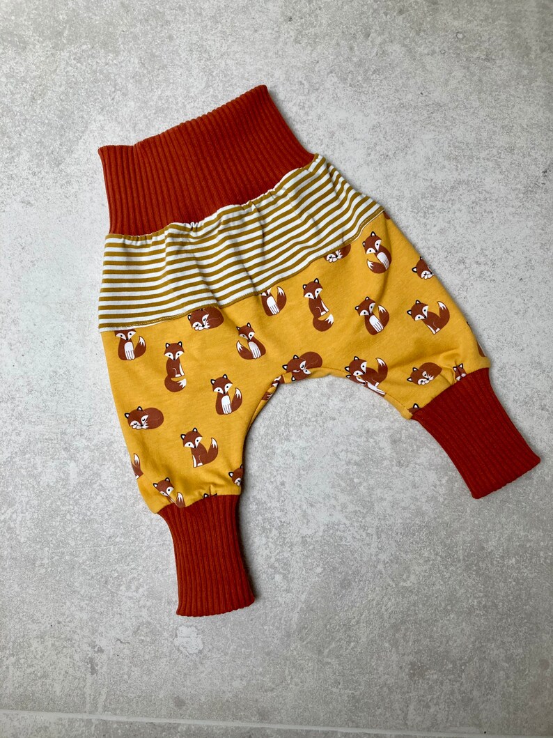 May include: A pair of yellow baby pants with a fox print and red ribbed cuffs and waistband.