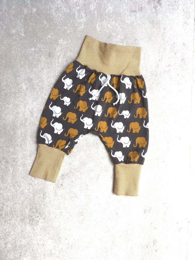 K&ouml;nnte beinhalten: Graue Babyhose mit einem wei&szlig;en und gelben Elefantenmuster. Die Hose hat einen braunen elastischen Bund und braune B&uuml;ndchen.