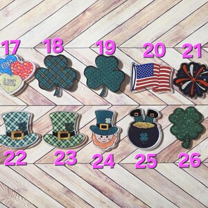 May include: A collection of decorative embellishments featuring various designs. Includes hearts with "XOXO" and "LOVE" text, shamrocks, an American flag, a firework, leprechaun hats, a leprechaun, a pot of gold, and a textured shamrock.