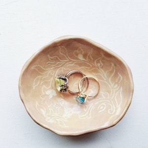 Glaserad handgjord liten lerskål. Skål med rosa blommiga prydnadssaker.
