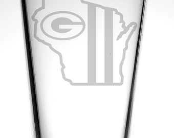 May include: A clear glass pint glass with a white outline of the state of Wisconsin and the Green Bay Packers logo etched on the side.