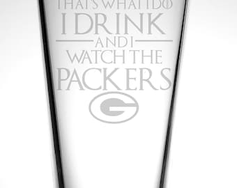 May include: A clear glass pint glass with the text "That's what I do I drink and I watch the Packers" and the Green Bay Packers logo etched on the side.