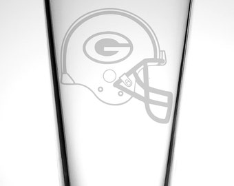 May include: A clear glass pint glass with a white etched design of a football helmet with a green "G" on the side.