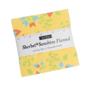 May include: A stack of yellow Sherbet Sunshine Flannel fabric squares with a floral pattern in orange, blue, and green. The fabric is wrapped with a white band that reads "Sherbet*Sunshine Flannel" and "by Corey Yoder of Coriander Quilts."