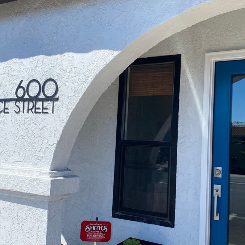 May include: A white building with a blue door and a black window. The building has a black metal address number that reads "600 CE STREET". There is a red sign with white text that reads "SMITH'S", "HUNGRY? GO WILD", and "2102 600 9210".