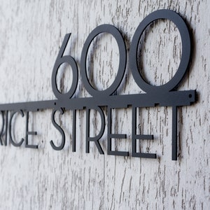 May include: Black metal house number sign with the number 600 and the words "Price Street" on a white textured wall.