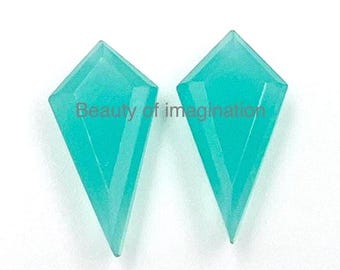 May include: Two teal blue gemstone cabochons cut in a diamond shape. The gemstones are faceted and have a pointed tip.