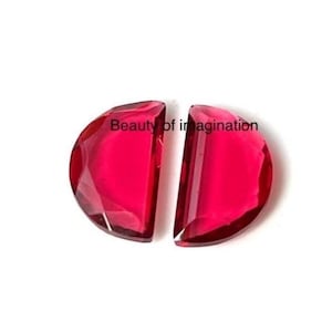 May include: Two half-circle shaped, faceted, deep red gemstones. The gemstones are cut to a flat edge, and the text "Beauty of imagination" is visible on the top.