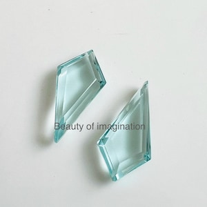 Puede incluir: Dos formas de diamante de vidrio facetado de color azul claro. Los diamantes son transparentes y tienen un ligero tono azul.