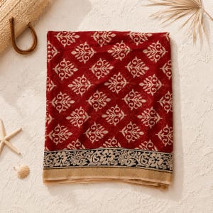May include: A rectangular fabric scarf in deep red featuring a repeating cream-colored botanical pattern. The bottom edge displays a wide black border with a detailed floral and paisley design, finished with a solid cream-colored hem at the base.