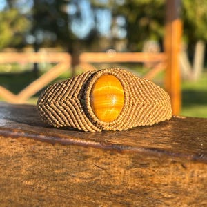 Peut inclure: Un bracelet en macramé doté d'une pierre précieuse œil-de-tigre ovale centrale avec un éclat chatoyant brun doré. Le bracelet est fabriqué à partir d'un cordon de couleur beige tissé dans un motif de nœuds en chevron dense.