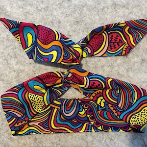 Puede incluir: Una diadema de tela colorida con un diseño anudado. La diadema presenta un patrón de remolino de rojo, azul, amarillo y blanco.