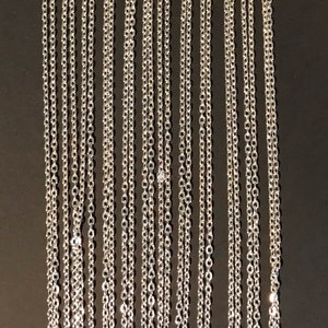 May include: A display of silver chain necklaces hanging on a white card. The chains are various lengths and are all the same style.