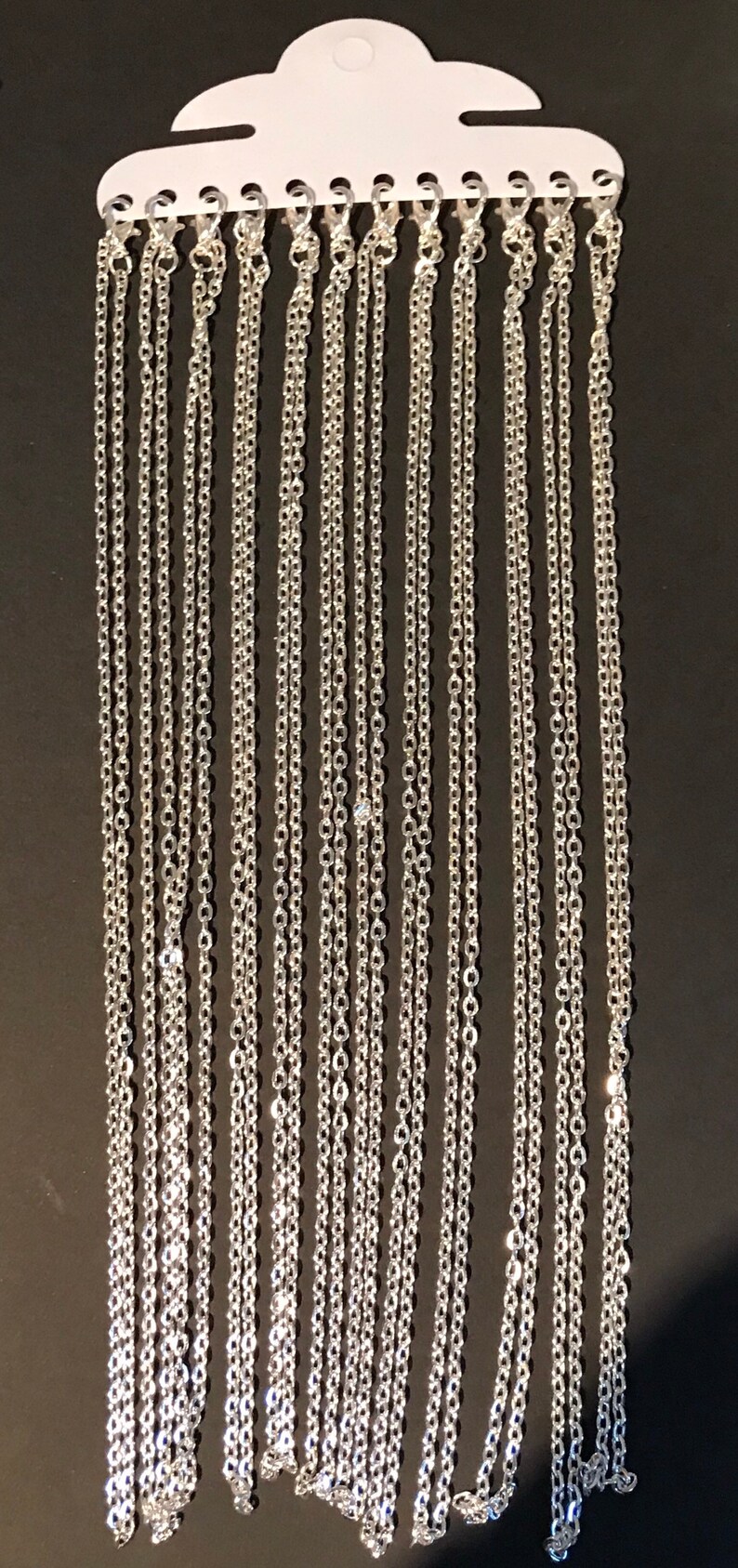 May include: A display of silver chain necklaces hanging on a white card. The chains are various lengths and are all the same style.