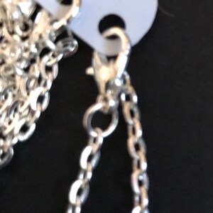 May include: Two silver chains with lobster claw clasps. The chains are hanging from a white tag.