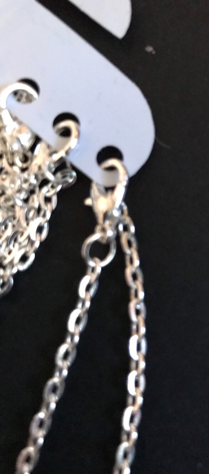 May include: Two silver chains with lobster claw clasps. The chains are hanging from a white tag.