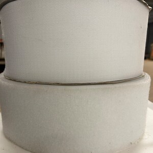 May include: Two rolls of white hook and loop fastener tape. The tape is on cardboard rolls.