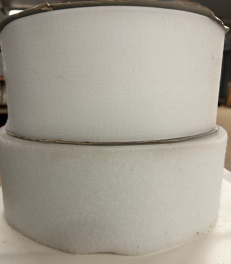 May include: Two rolls of white hook and loop fastener tape. The tape is on cardboard rolls.