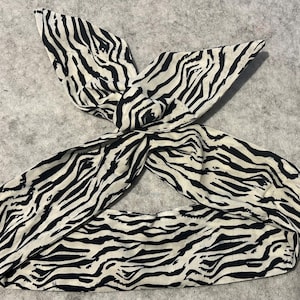 Può includere: Un cerchietto con stampa zebrata in bianco e nero. Il cerchietto è realizzato in tessuto morbido ed è annodato nella parte superiore.