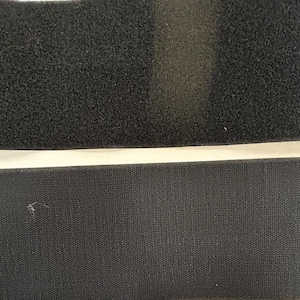 May include: Two strips of black hook and loop fastener, also known as Velcro. The top strip has a fuzzy texture, while the bottom strip is smooth.
