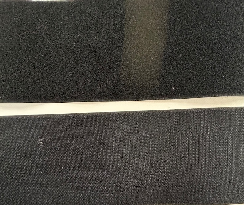 May include: Two strips of black hook and loop fastener, also known as Velcro. The top strip has a fuzzy texture, while the bottom strip is smooth.