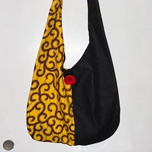 May include: A black and yellow fabric tote bag with a red button. The bag has a swirl pattern on one side and is plain black on the other side.