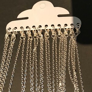 May include: A pack of 15 silver chains with lobster clasps. The chains are hanging from a white card with holes for each chain.