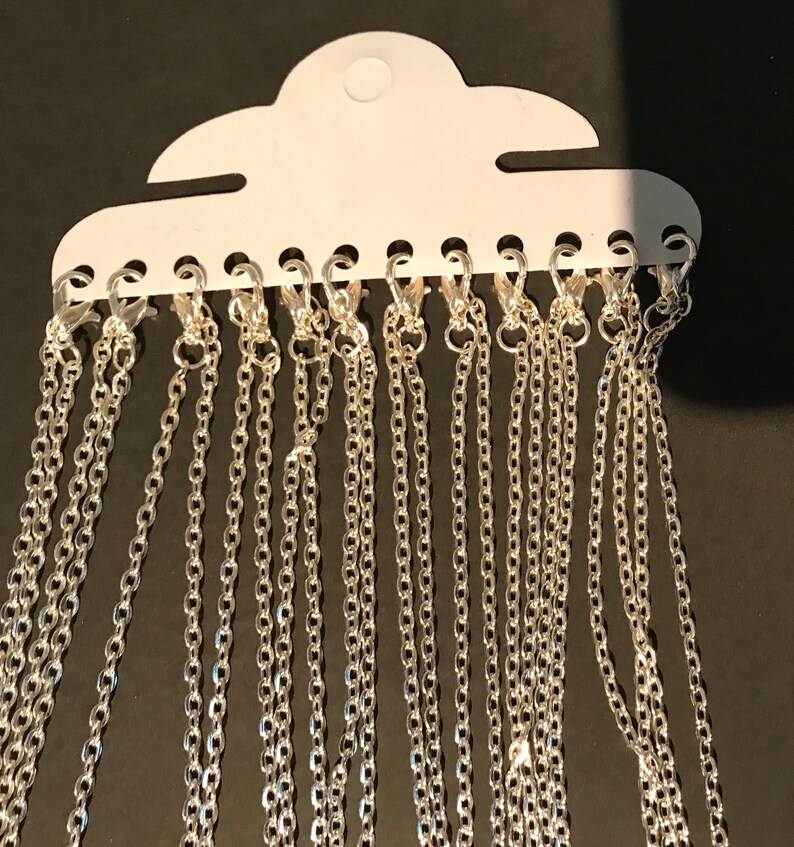 May include: A pack of 15 silver chains with lobster clasps. The chains are hanging from a white card with holes for each chain.