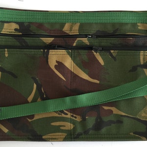 Può includere: Un grembiule in tessuto mimetico con due tasche con cerniera e una cinghia regolabile verde.