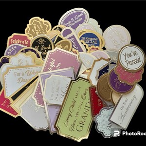 May include: A collection of gold and silver gift tags with various celebratory messages, including "Celebrate", "You've Passed", "For a Wonderful Daughter", and "Every Child Has a Granda".