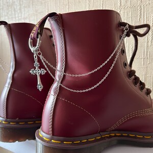 May include: A pair of burgundy leather boots with silver chains and cross charms attached to the back of the boots.