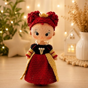 May include: A handcrafted crochet doll featuring a queen character with voluminous dark red hair, a small gold crown, and a black bodice with white pearl accents. The doll wears a long red skirt with a textured yellow overlay and striped sleeves.