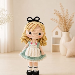May include: A handcrafted crochet doll featuring blonde curly hair with a black headband, wearing a light blue dress with a white apron, two small red buttons, and black shoes with white socks. The doll has round black eyes and pink cheeks.